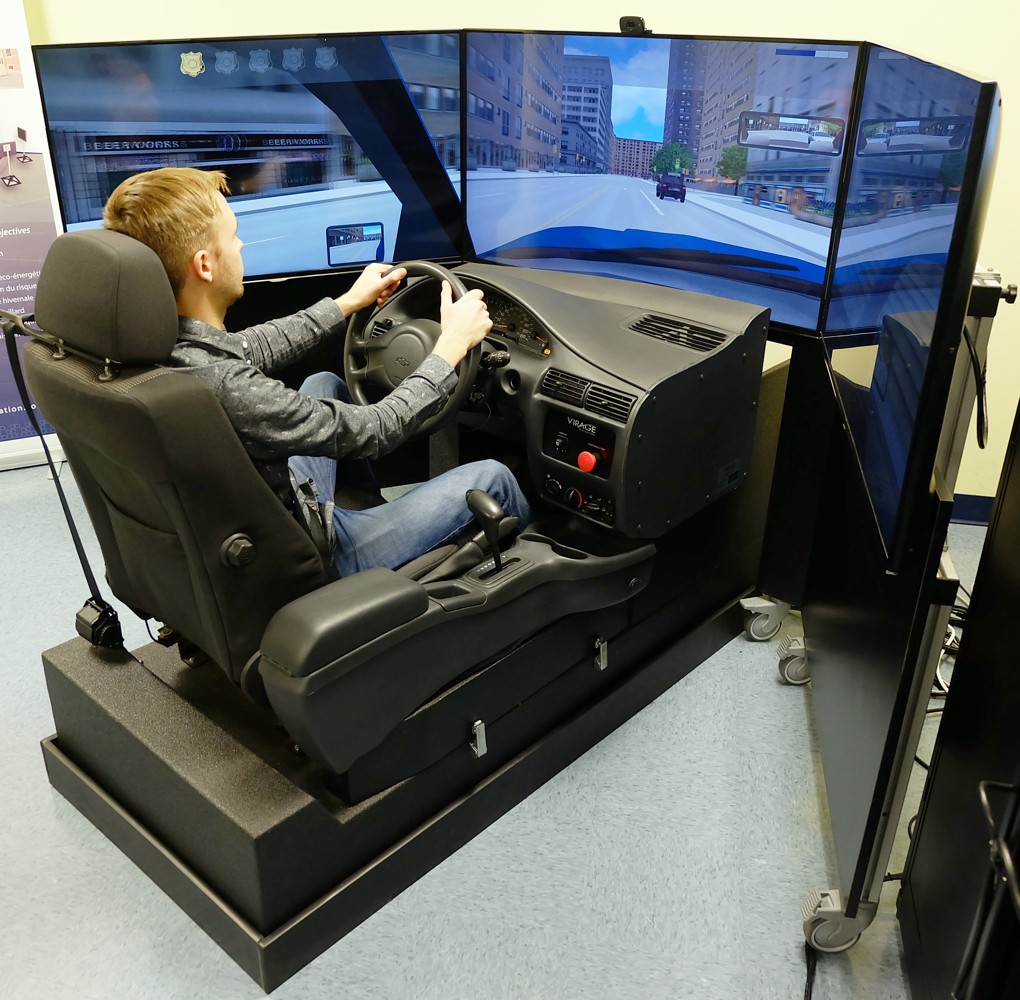 Driver in a Virage Simulation vehicle cockpit with steering wheel, gear selector and three road-simulation screens